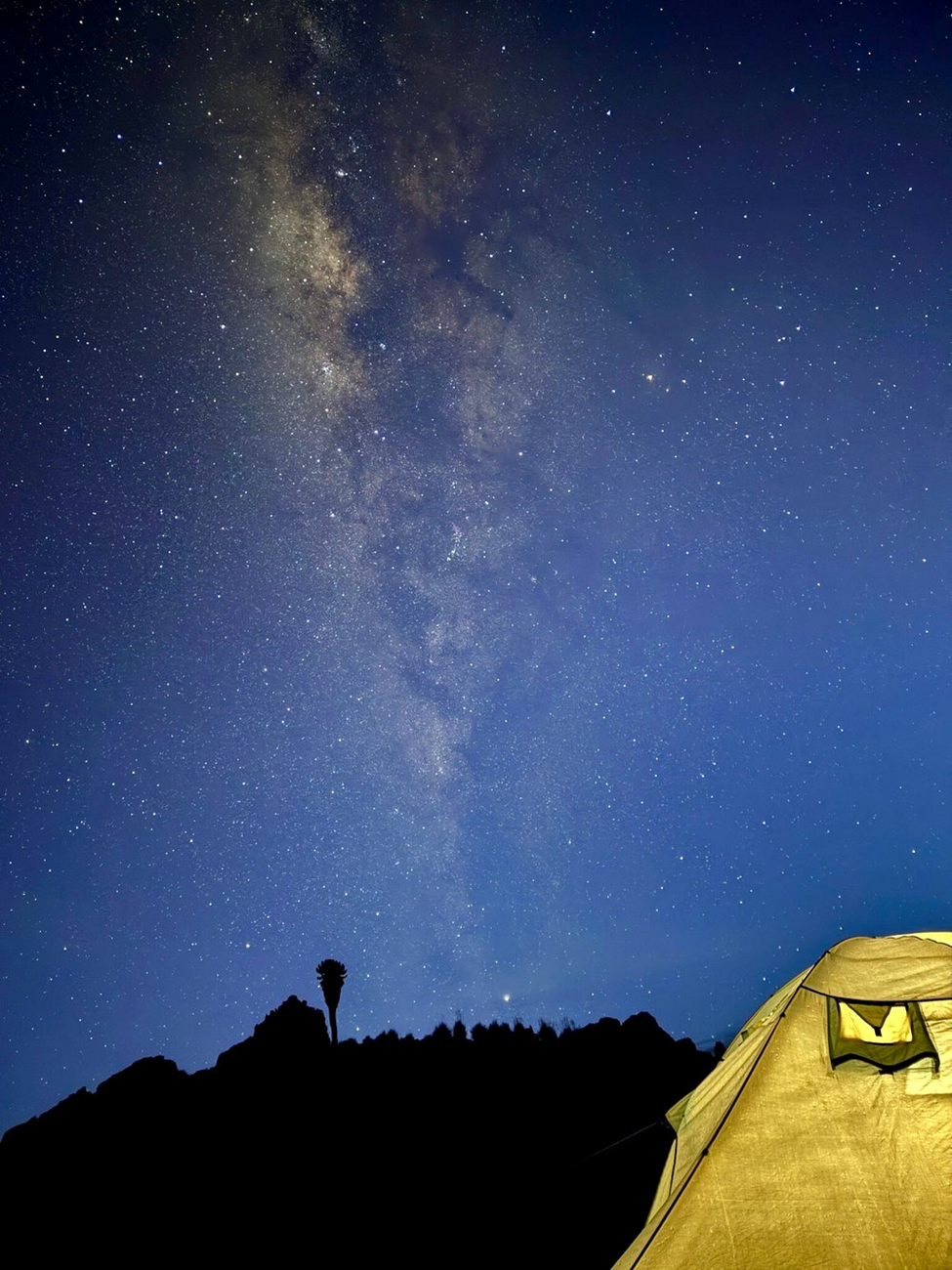 A tent lit up from inside with the Milky Way spiral arm shining at night on Mount Kenya